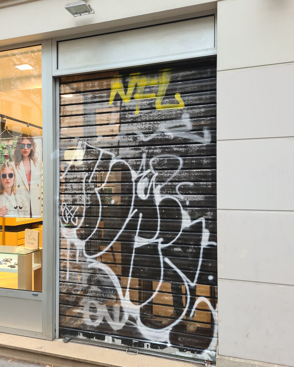 Rideau métallique perforé d'un commerce à Paris avec des tags et graffitis